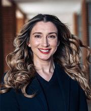 Patricia Morchel smiling with long wavy brown hair wearing a navy blue blazer with navy blue v-neck top under it